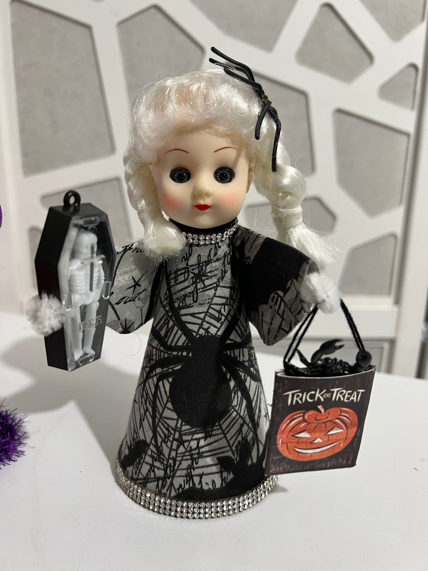 Spider themed vintage looking doll with trick or treat bag on white table.