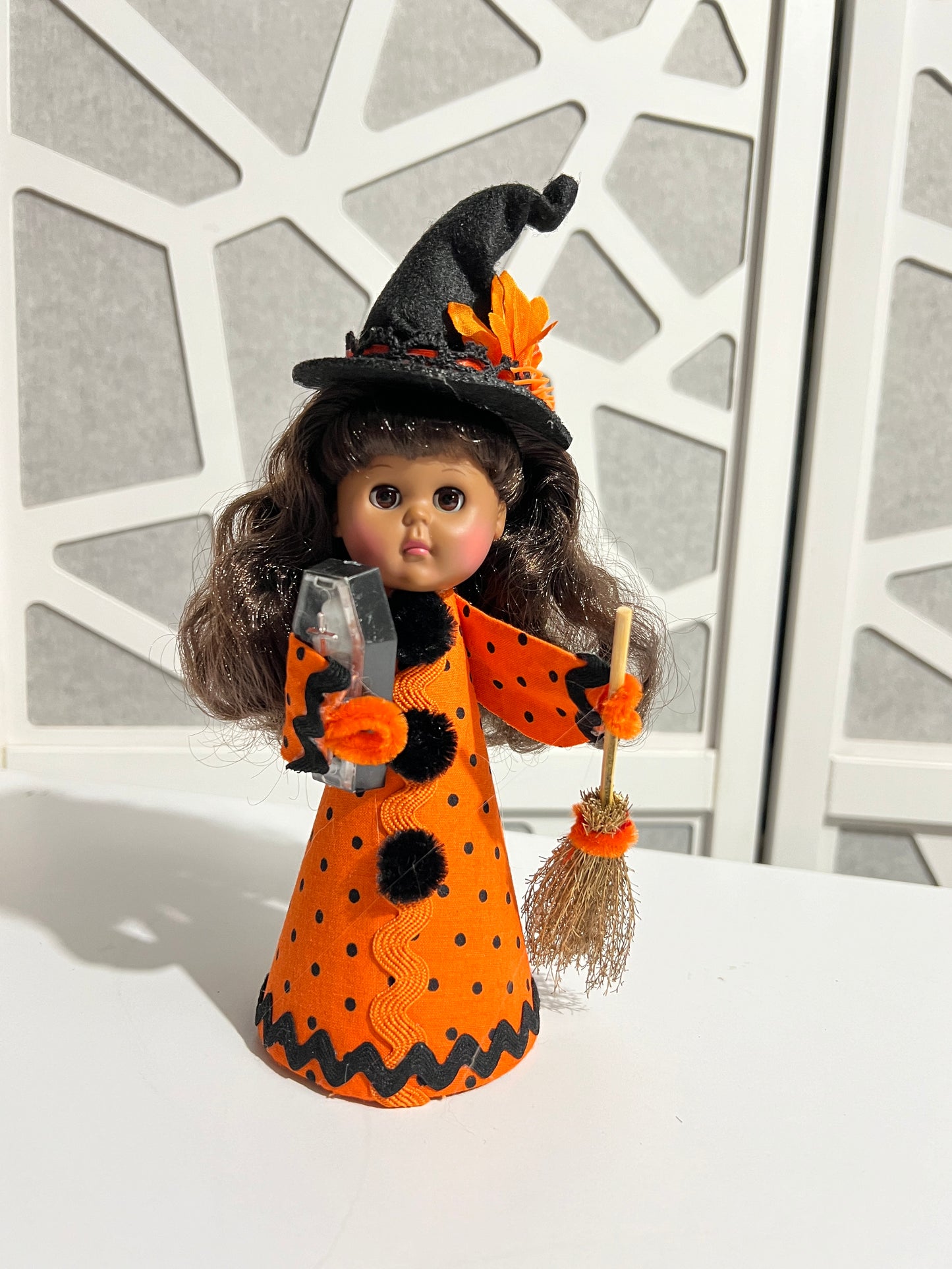 Witch doll in orange and black polka dot outfit with broom adn skeleton toy on white table.