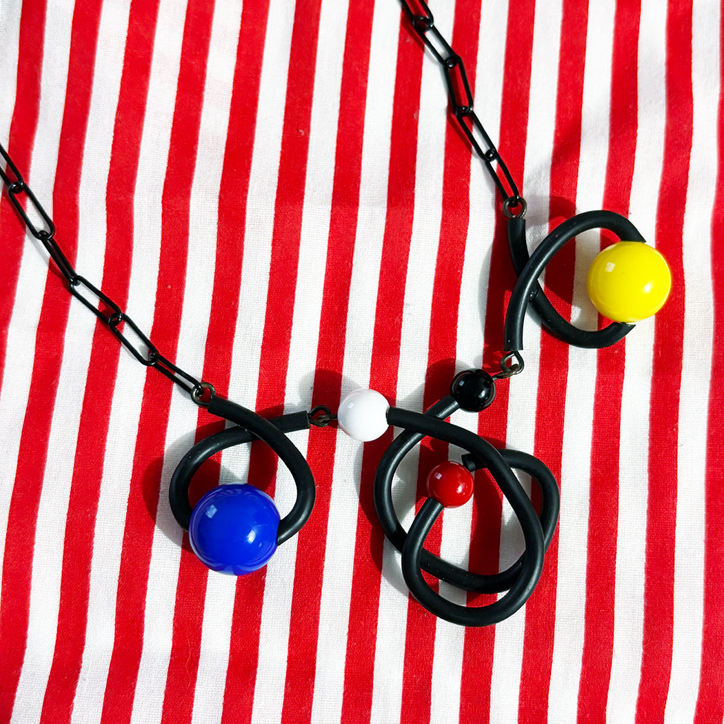 Colorful Bounce necklace in black with yellow, black, red, and white multisized beads on black enamel chain from Audacious Studio.