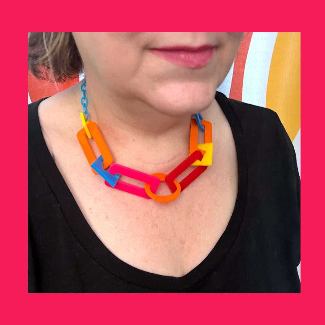 Person wearing a colorful necklace with a pink background