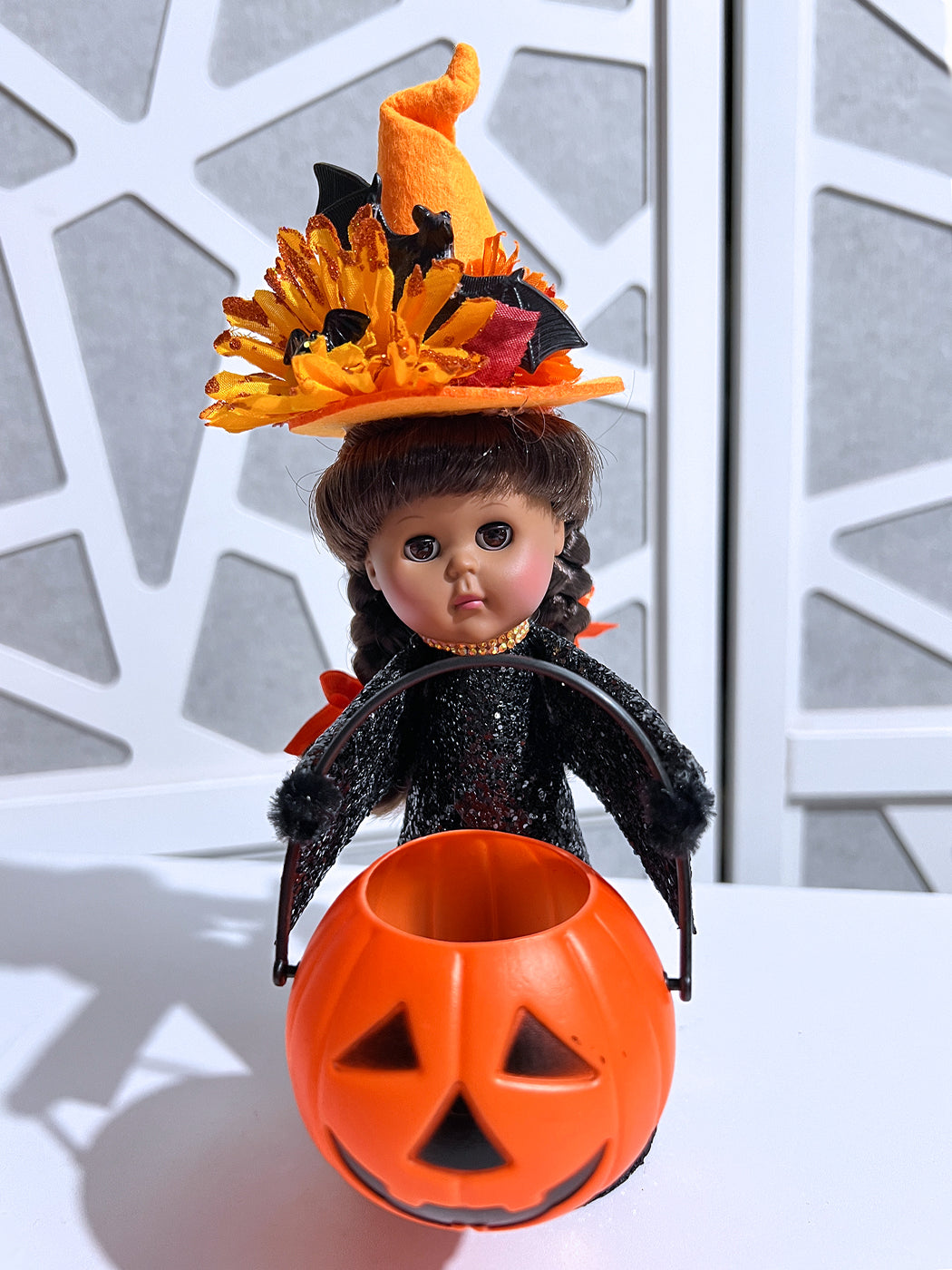 Halloween-themed doll with a witch hat and pumpkin bucket against a decorative background