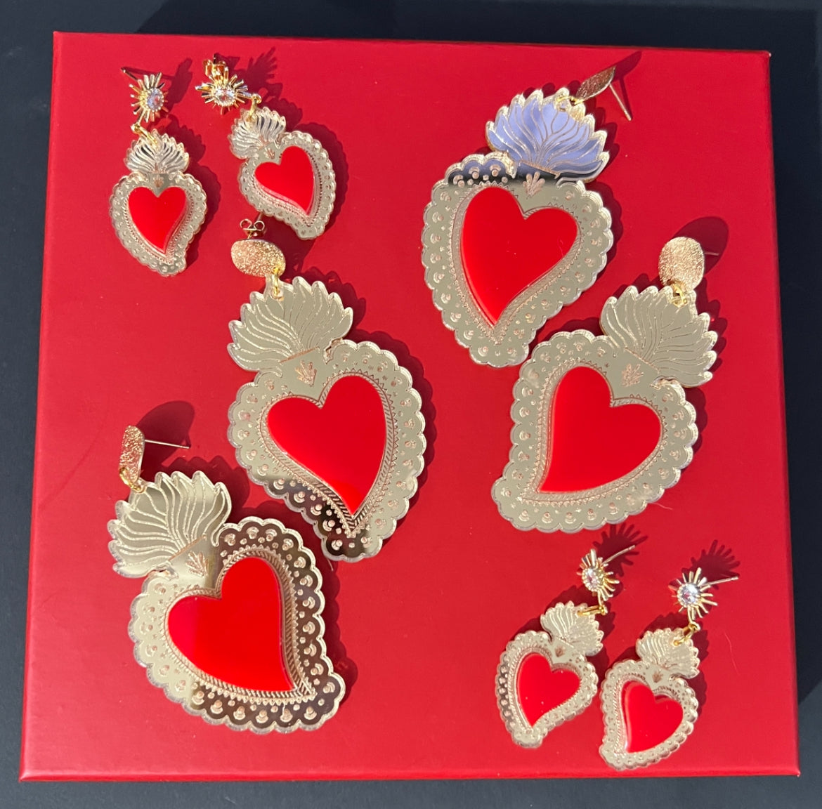 A collection of acrylic sacred heart earrings on a red background.