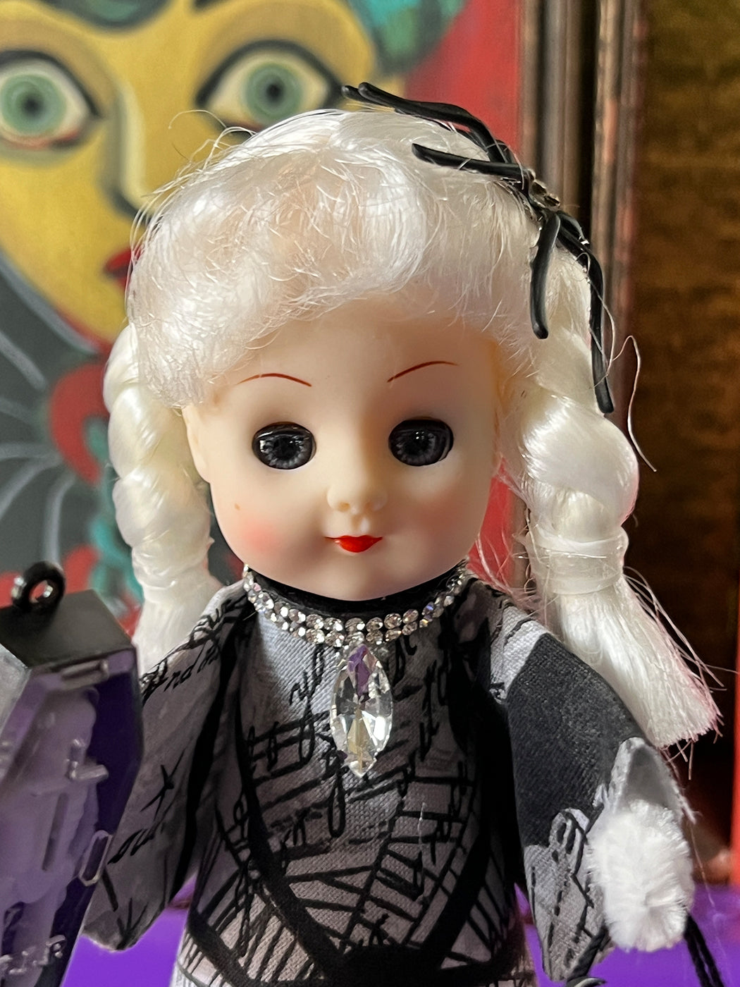 Vintage-style doll with white hair and black dress against a colorful abstract background