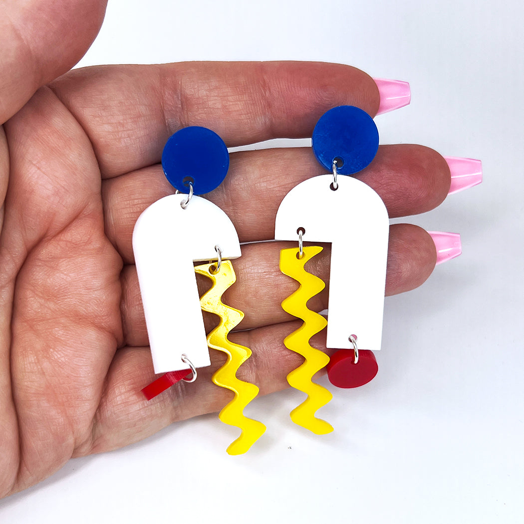 Hand holding Arch Mobile Modernist art earrings in white, red, blue and yellow.