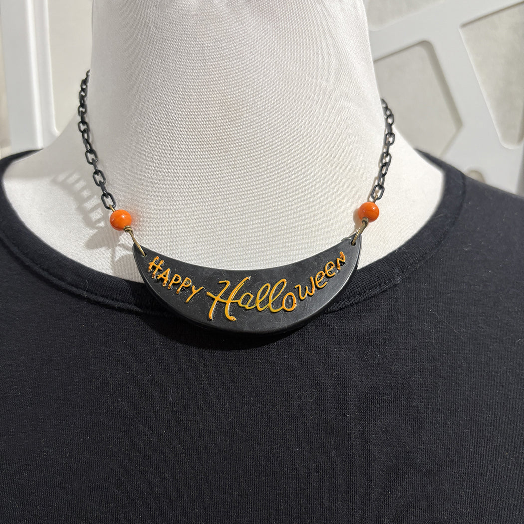 Black 'Happy Halloween' necklace with orange beads on a mannequin wearing a black shirt.