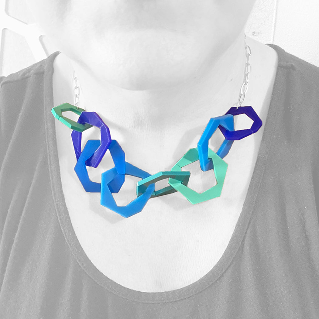 Necklace with blue and turquoise geometric links on a mannequin wearing a gray tank top.