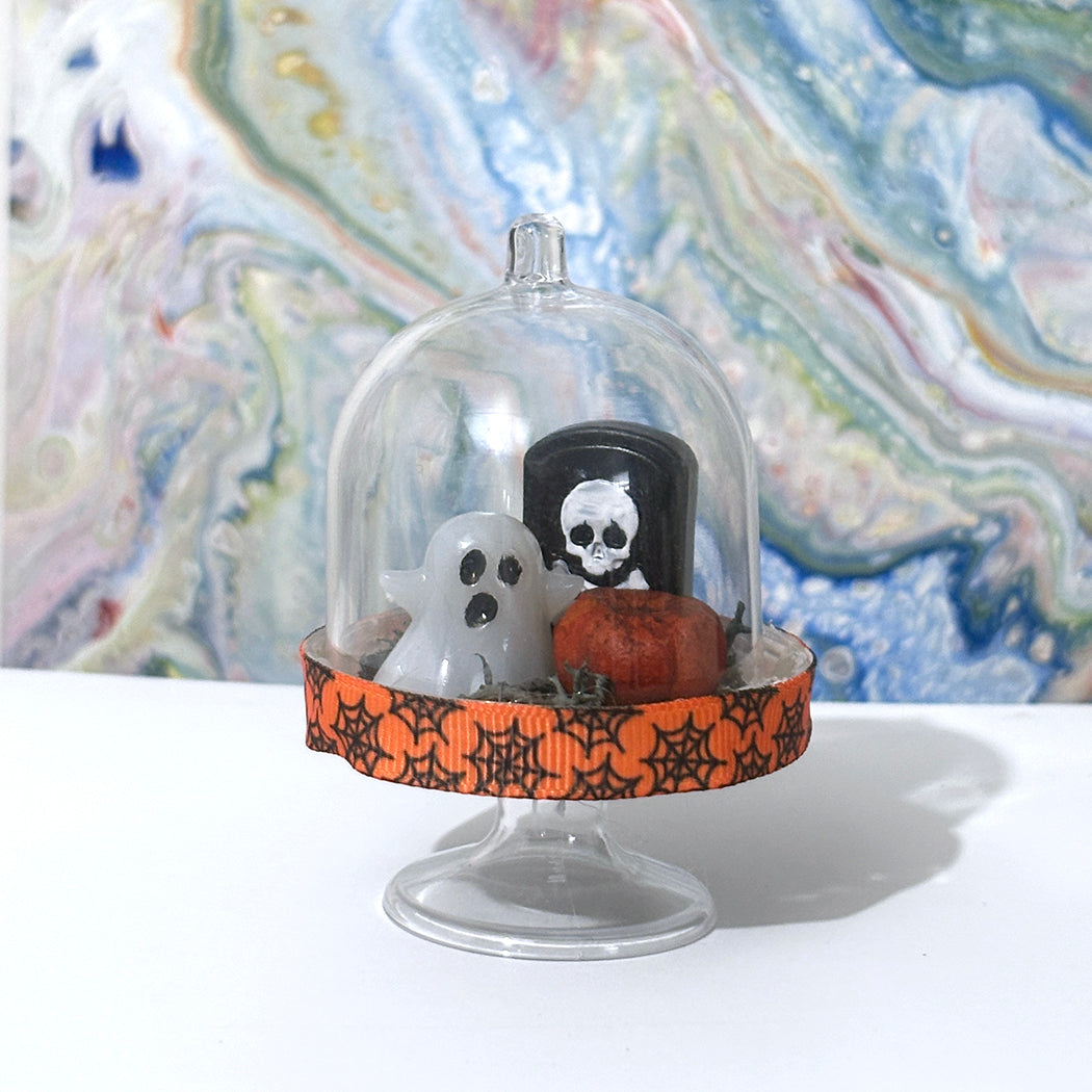 Halloween-themed display u with ghost and tombstone figurines on an abstract background.