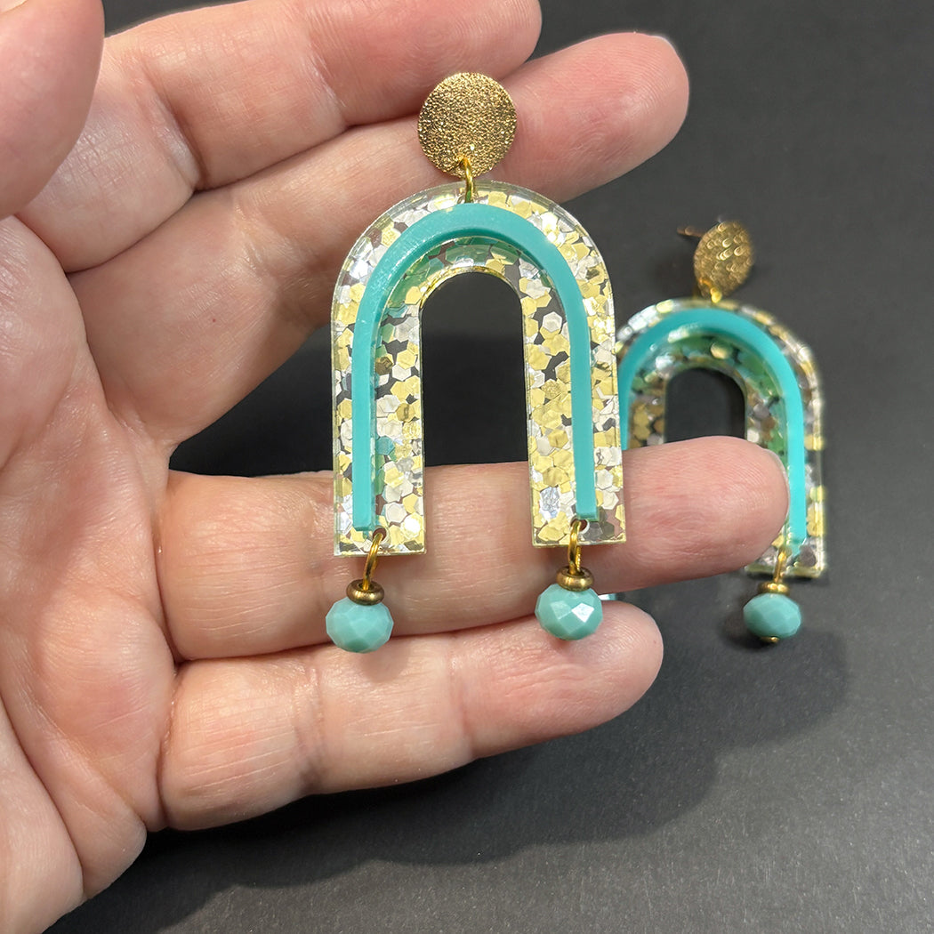 Hand holding gold glitter with turquoise accent arch post earrings from Audacious Studio.