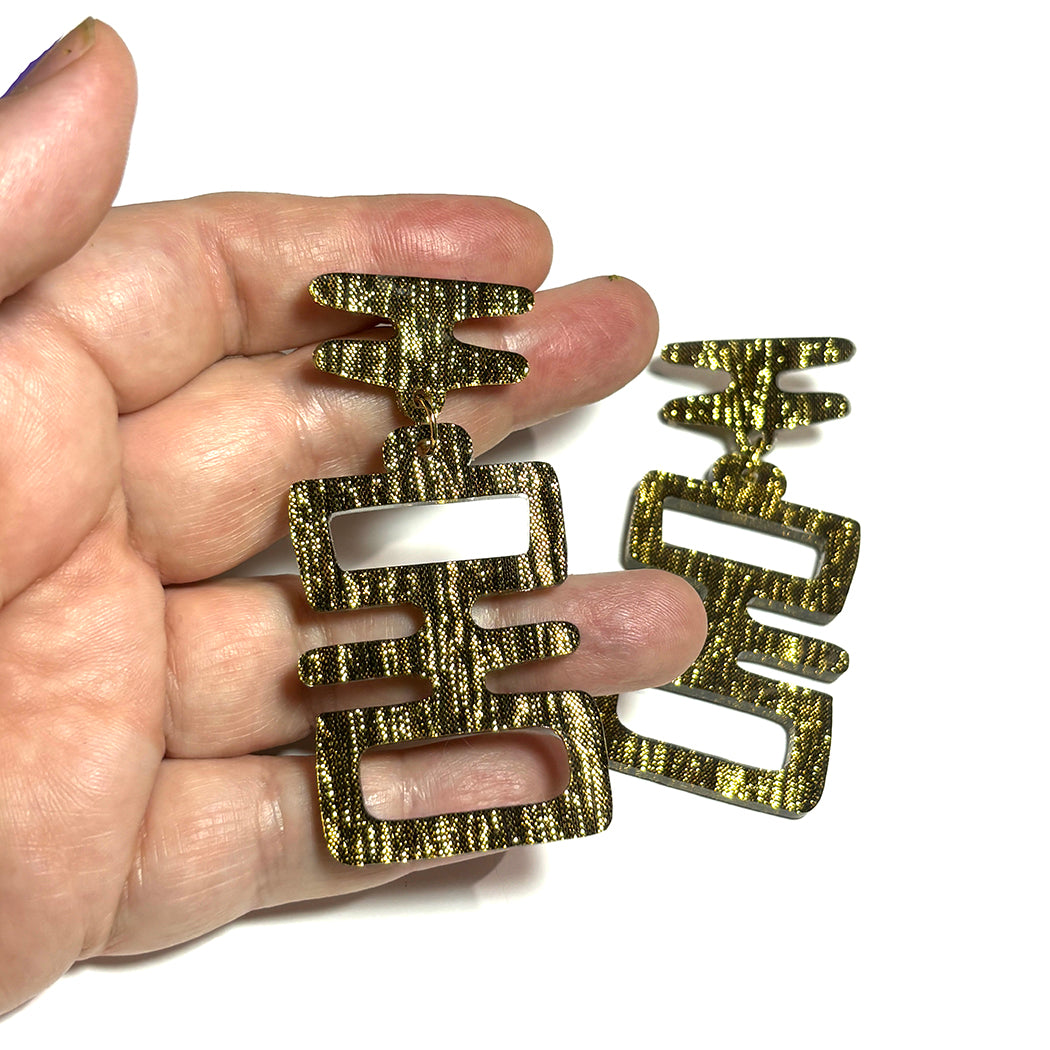 Hand holding Golden Idol statement earrings from Audacious Studio.