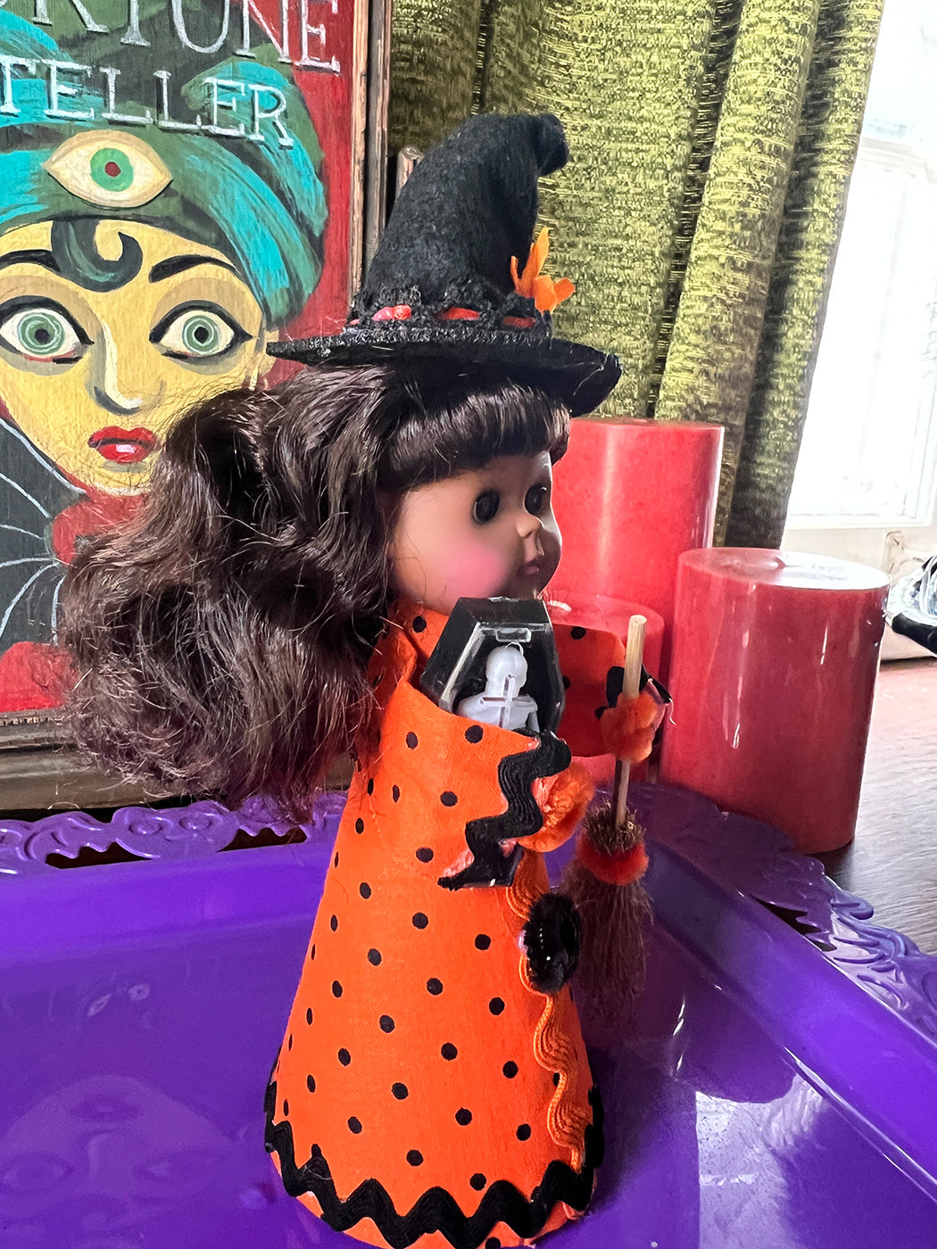 Halloween-themed doll with witch outfit and broom on a purple surface.