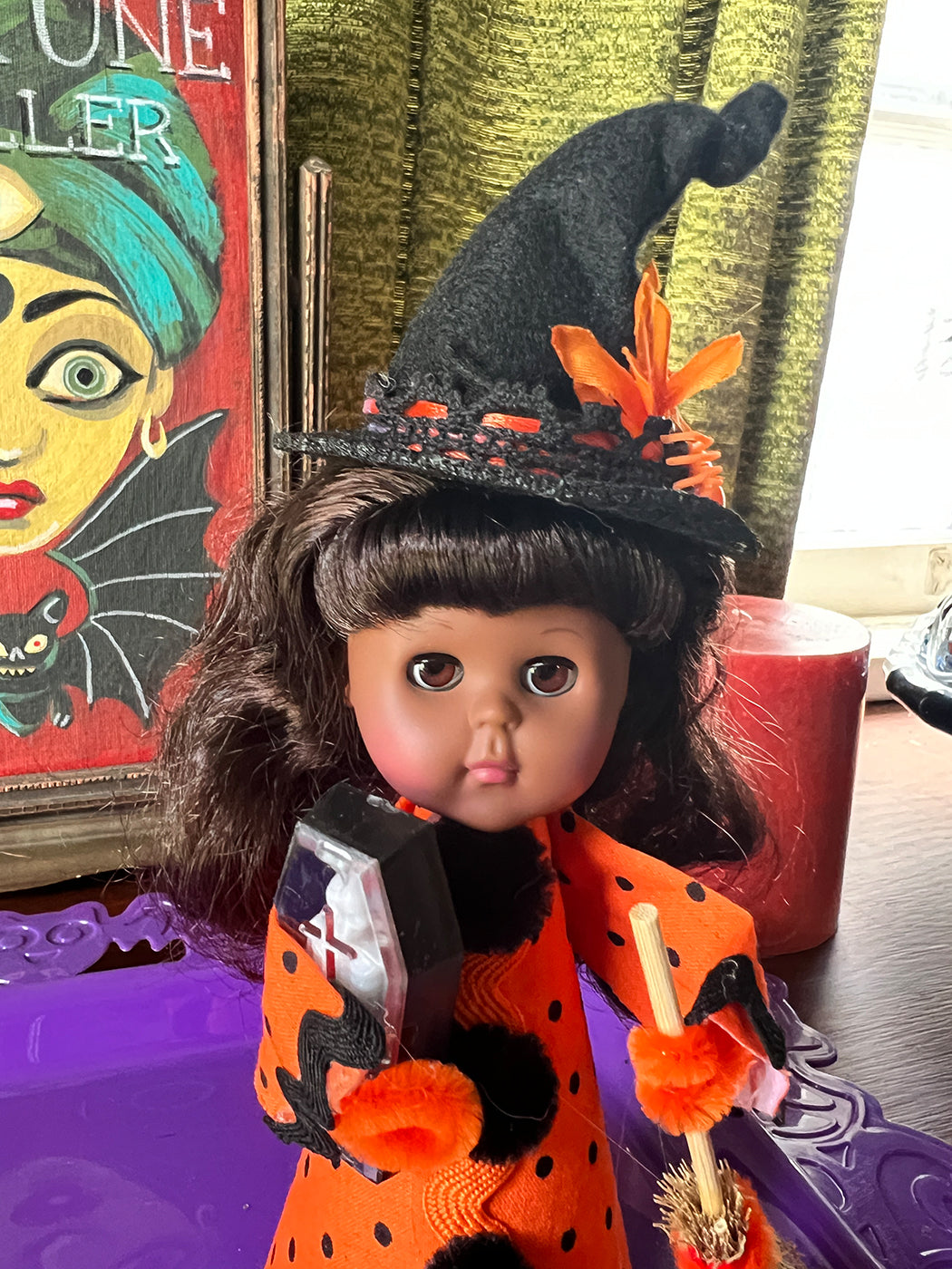 Halloween-themed doll with witch costume and hat on a table with decorations.