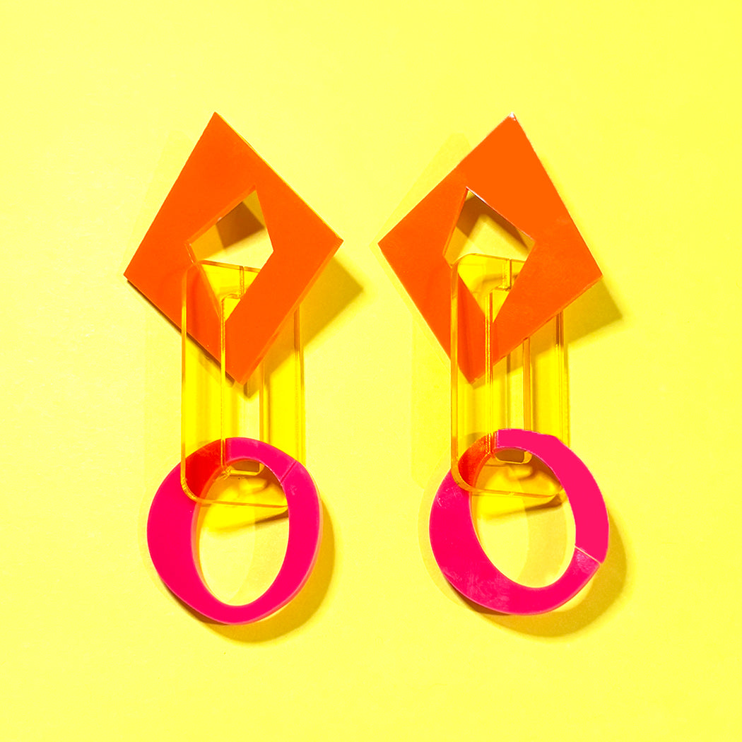 Chunky geometric chain link earrings in orange, clear yellow and hot pink from Audacious Studio on yellow background.