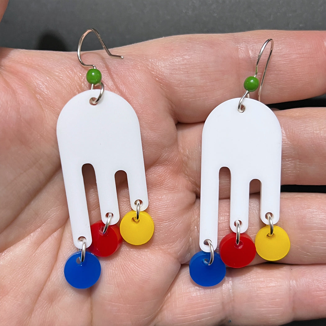 Hand holding 30s inspired Nora Drip Mobile earrings. Classic retro earrings in white, yellow, red and blue for all vintage fashionistas from by Barbe Jewelry.