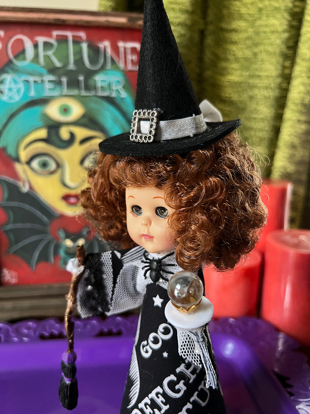 Vintage-style doll with witch outfit and hat in front of a colorful 'Fortune Teller' sign.