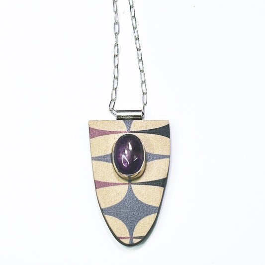 A shield-shaped pendant with a geometric pattern in purple and cream colors, featuring a large amethyst accent in the center, attached to a metal chain.