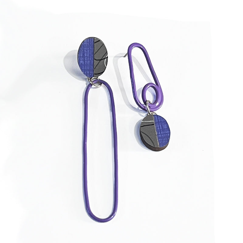 Close of of asymetrical purple and gray laminate and powdercoated earrings on white background.
