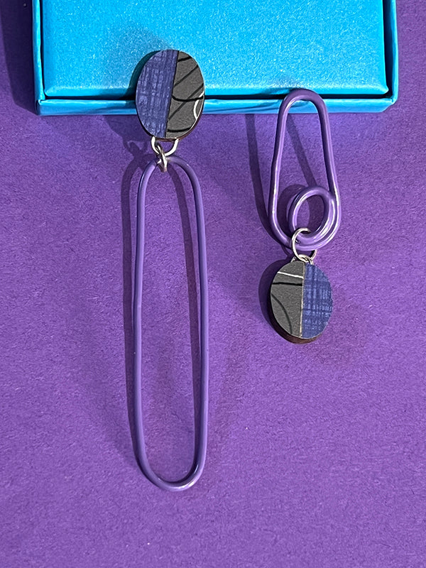 Close of of asymetrical purple and gray laminate and powdercoated post earrings on purple background.