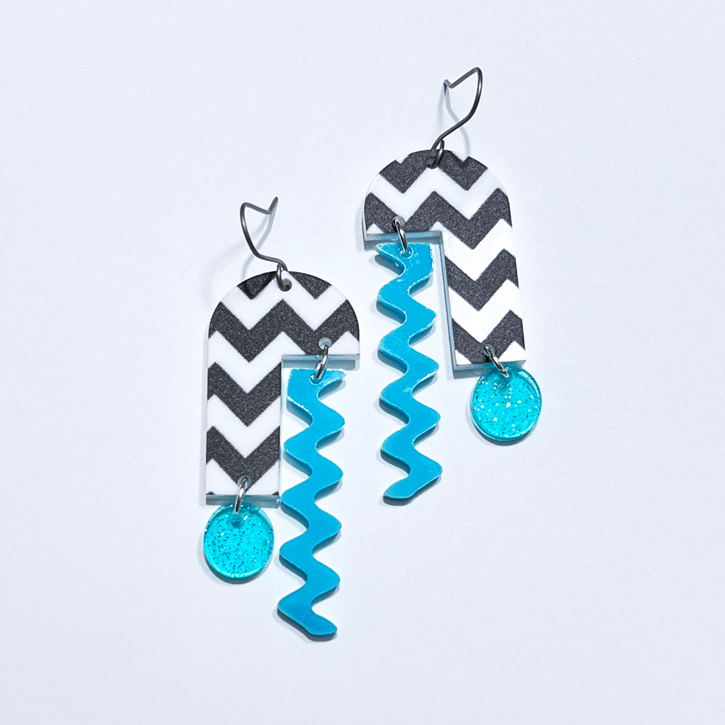 Black and white chevron patterned arch mobile earrings with blue dangles.