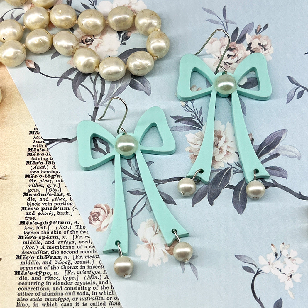 Large aqua acrylic bow with faus pearl center and faux pearl droplets on a background of vintage papers