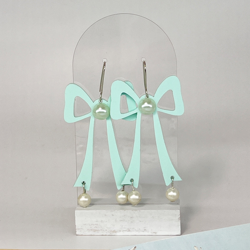 Large aqua acrylic bow earrings with faus pearl center and faux pearl droplets on a clear acrylic display stand. 