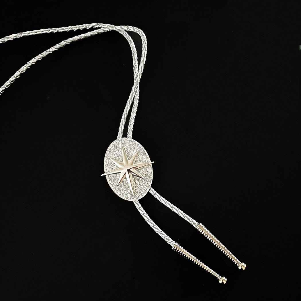 A silver-toned western bolo necklace featuring an oval starburst pendant suspended on silver braided cords against a solid black background.