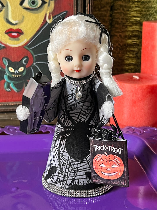Vintage-style doll in Halloween costume with 'Trick-or-Treat' bag on a purple surface.