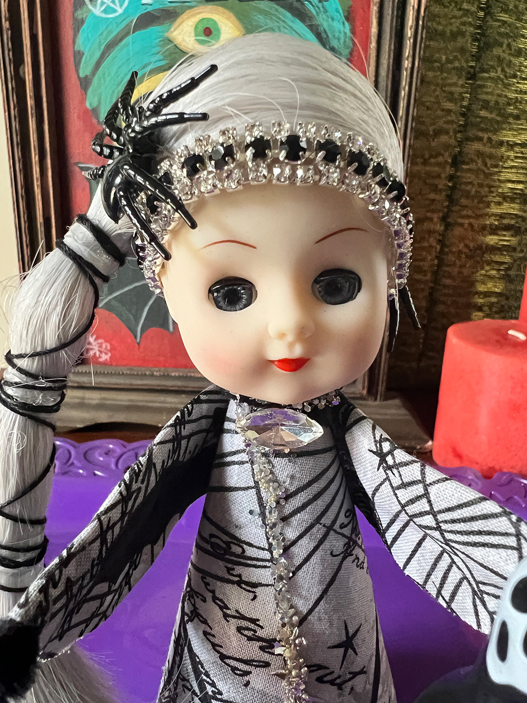 Vintage-style Halloween doll with decorative headpiece and spider costume, set against a colorful background.