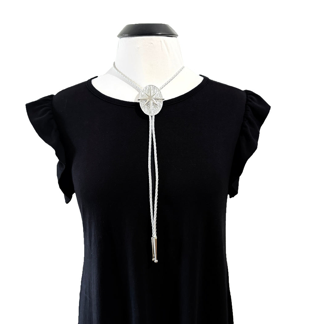 A silver-toned bolo tie necklace with a textured circular pendant and braided cord, displayed on a black dress form wearing a black top against a white background.