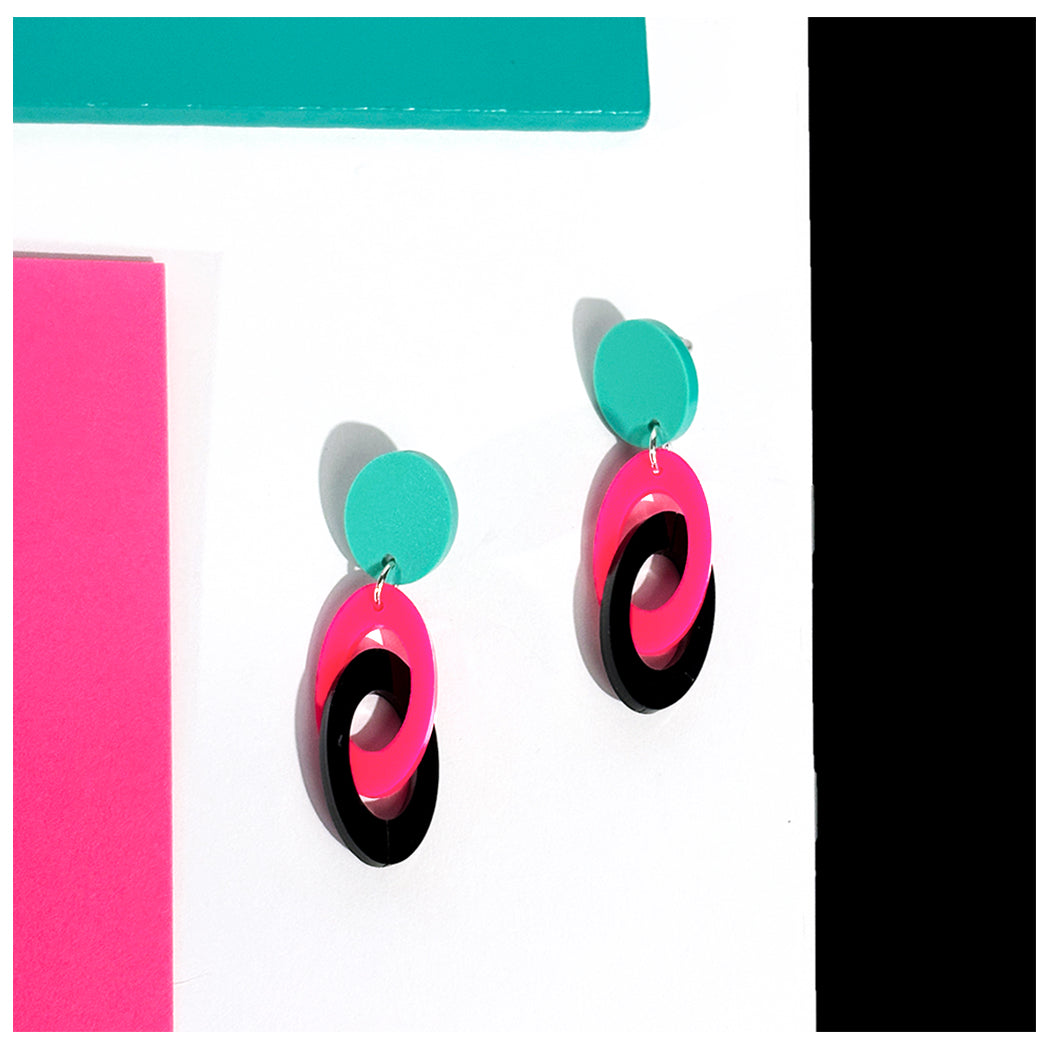 Colorful earrings with Hot pink, black, and aqua oval design on a white background.