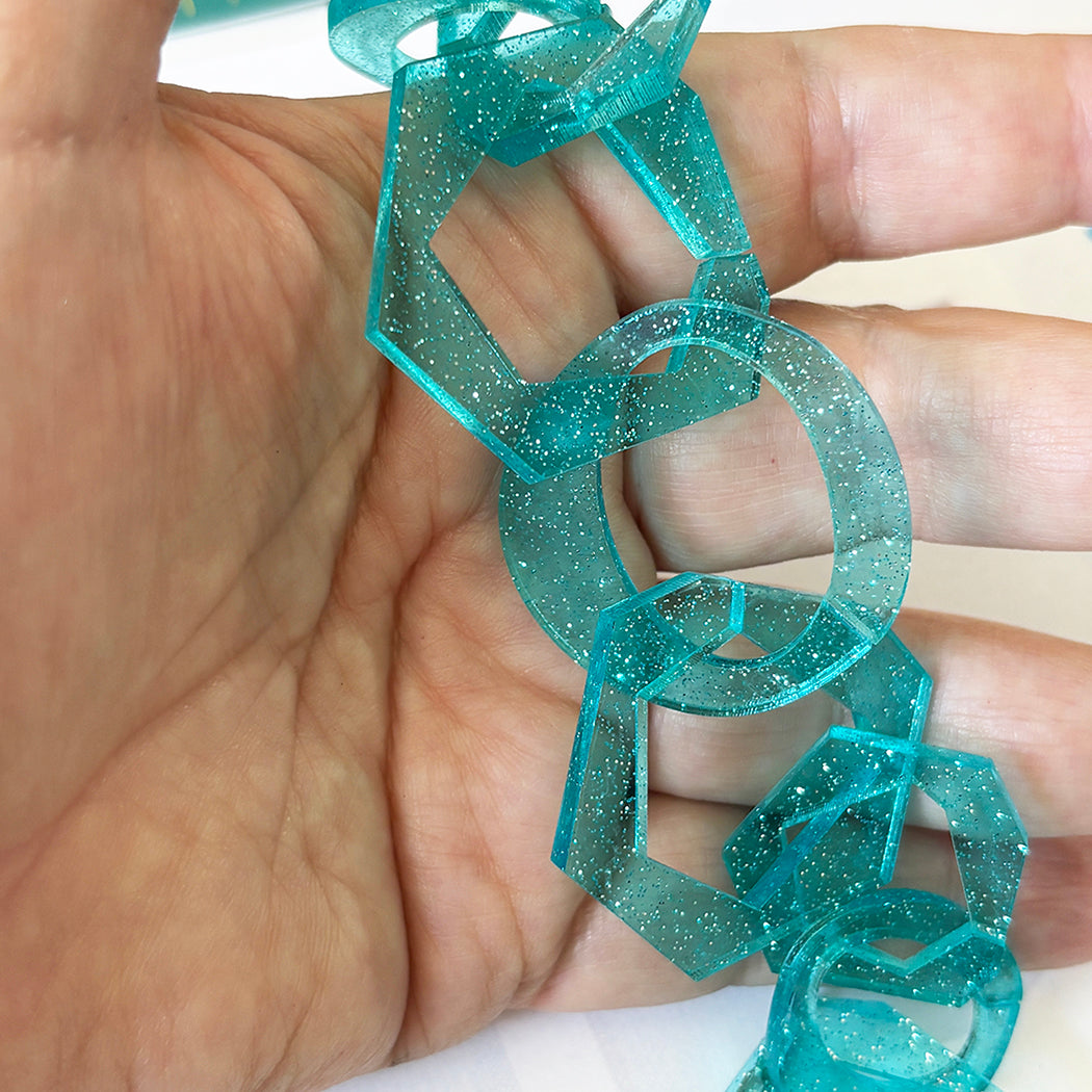 Turquoise glittery chain held in a hand against a neutral background