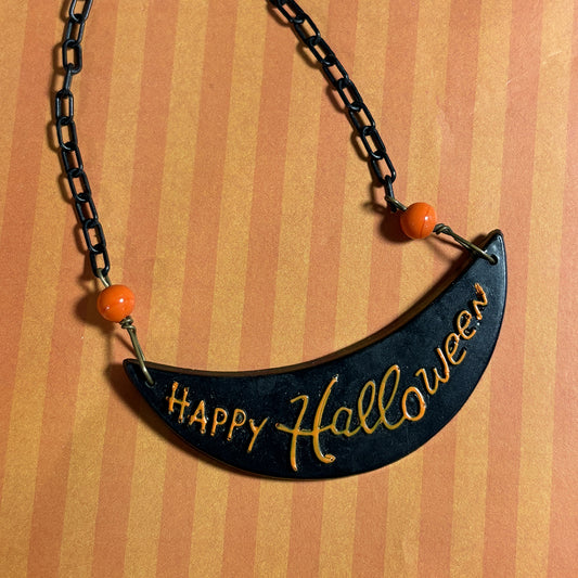 Black 'Happy Halloween' necklace with orange beads on a striped background