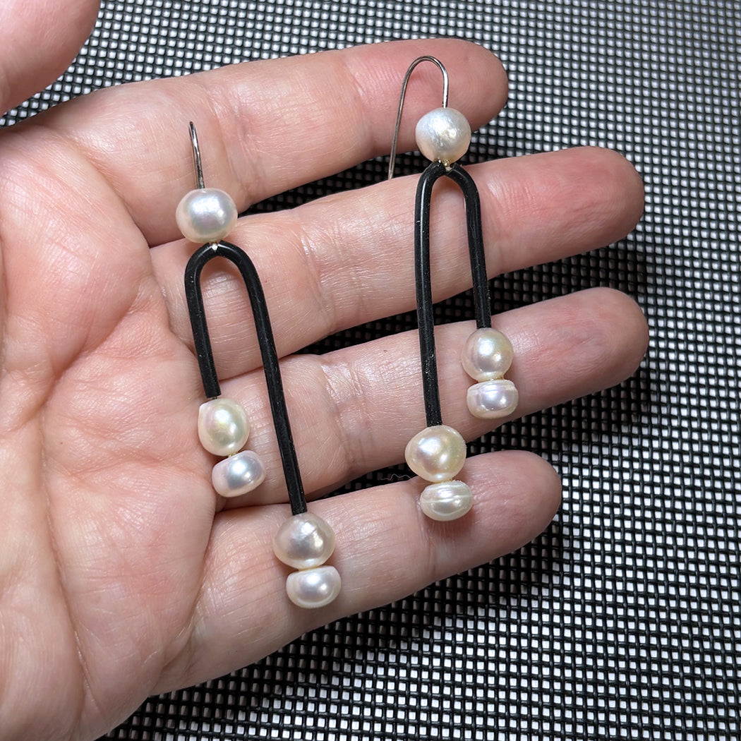 Hand holding Post Modern Pearl earrings featuring fresh water pearls and black rubber. 