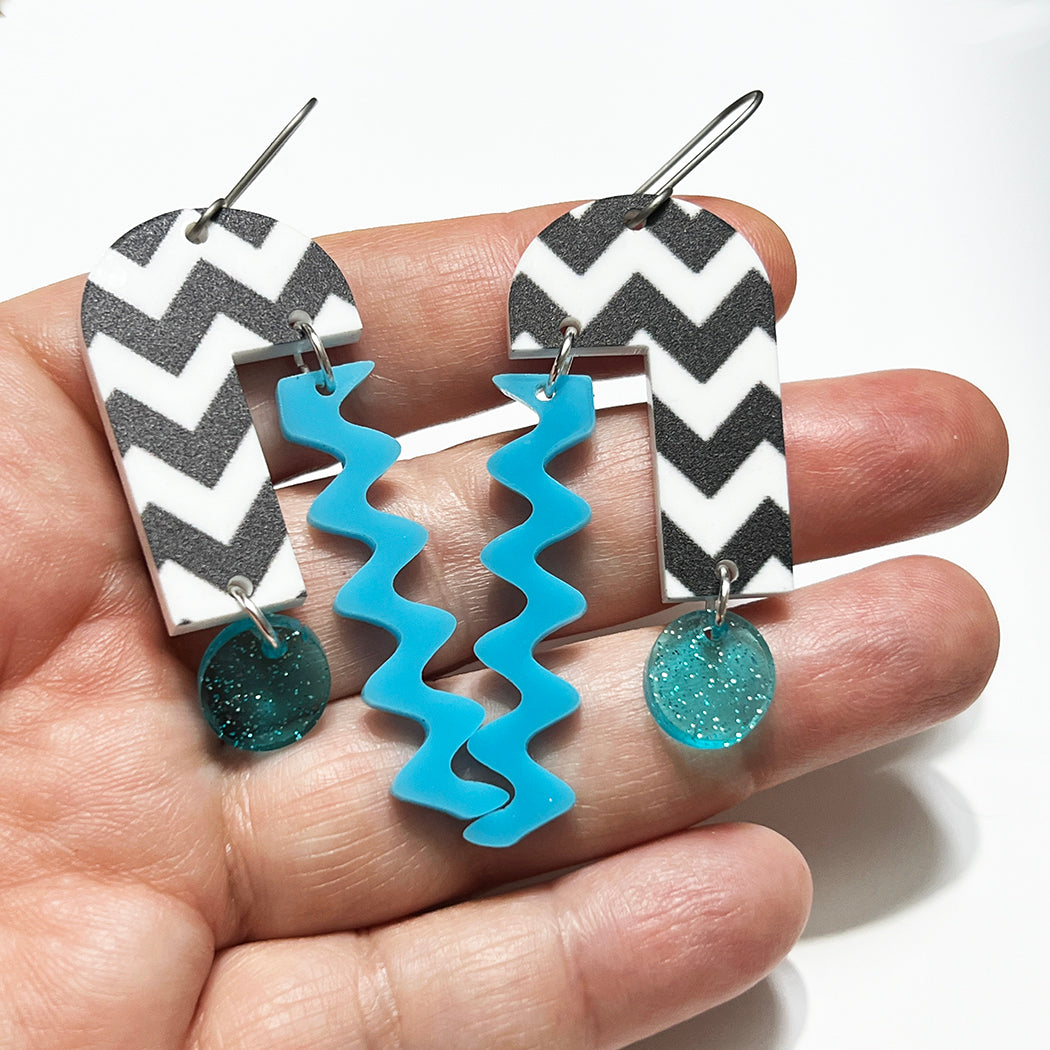 Hand holding geometric midcentury inspired arch mobile earrings
