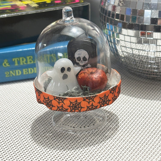 Halloween-themed display with ghost, skull, and pumpkin under a plastic dome