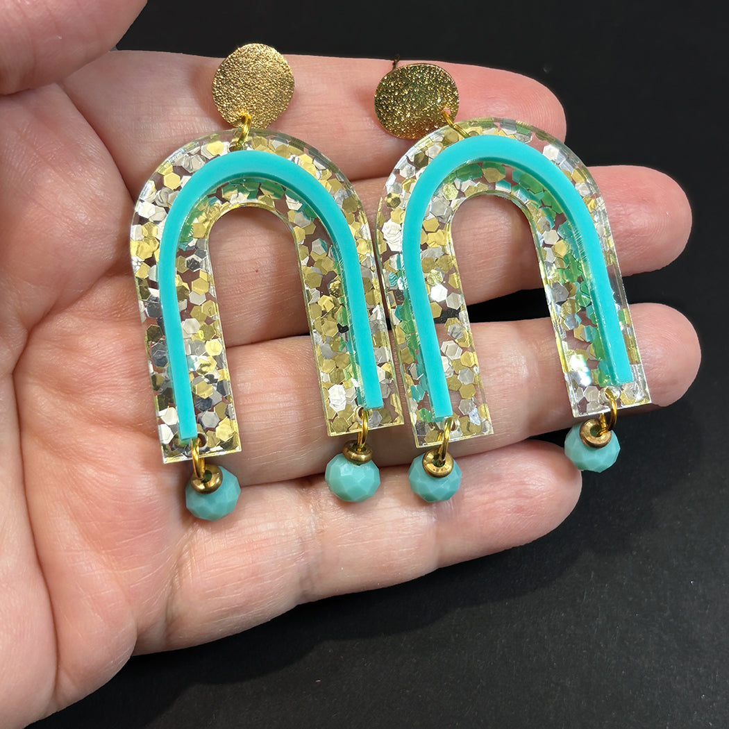 Hand holding Golden Girls Glitter Arch Earrings from Audacious Studio.
