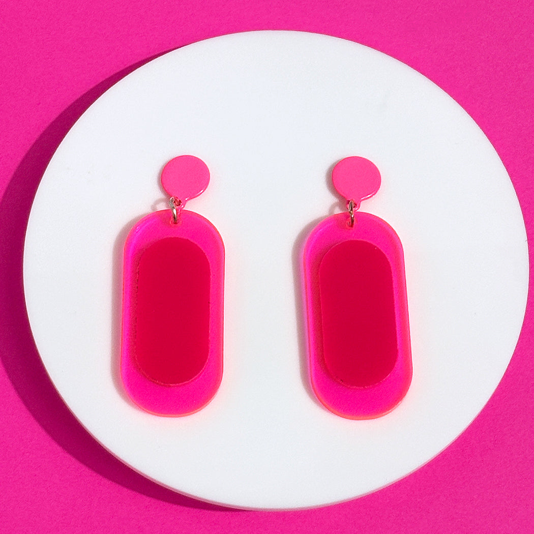 Hot pink, colorblock oval earrings on a round white display with a pink background.