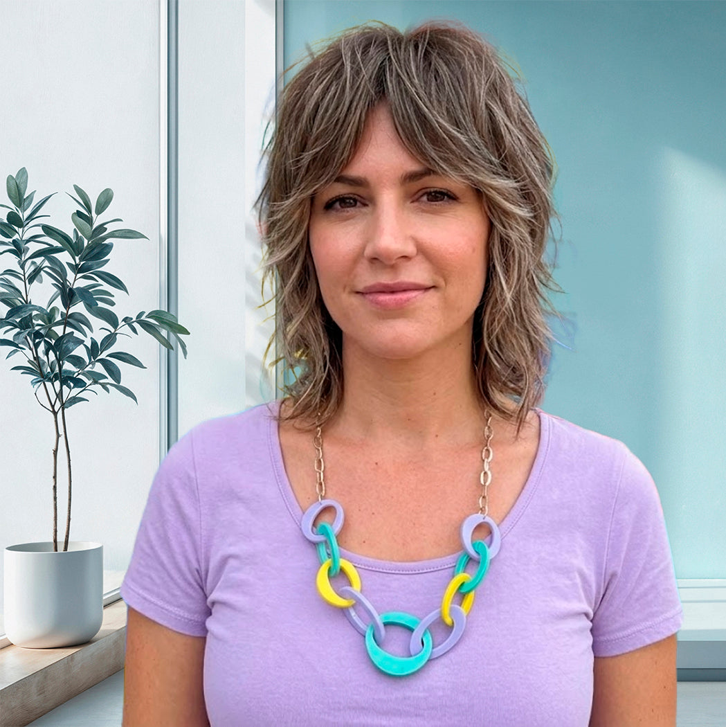 Woman wearing a colorful necklace in front of a window with a plant.