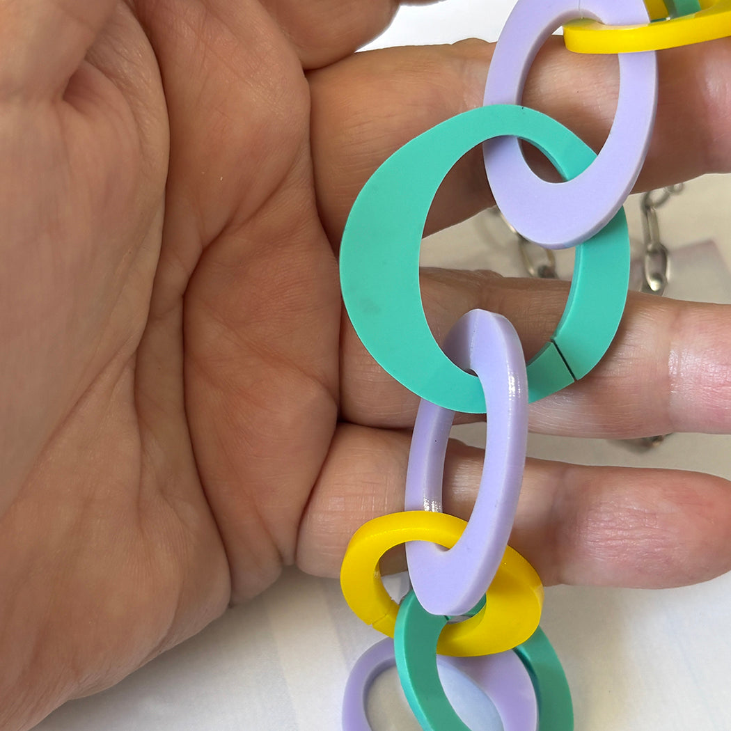 Aqua, lavender and yellow abstract link chain necklace held in a hand against a neutral background