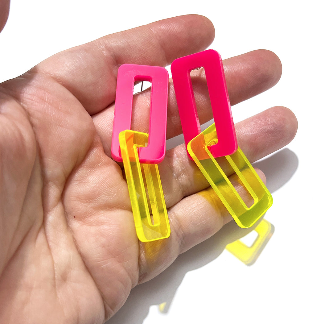 Hand holding hot pink and neon yellow large link earrings.
