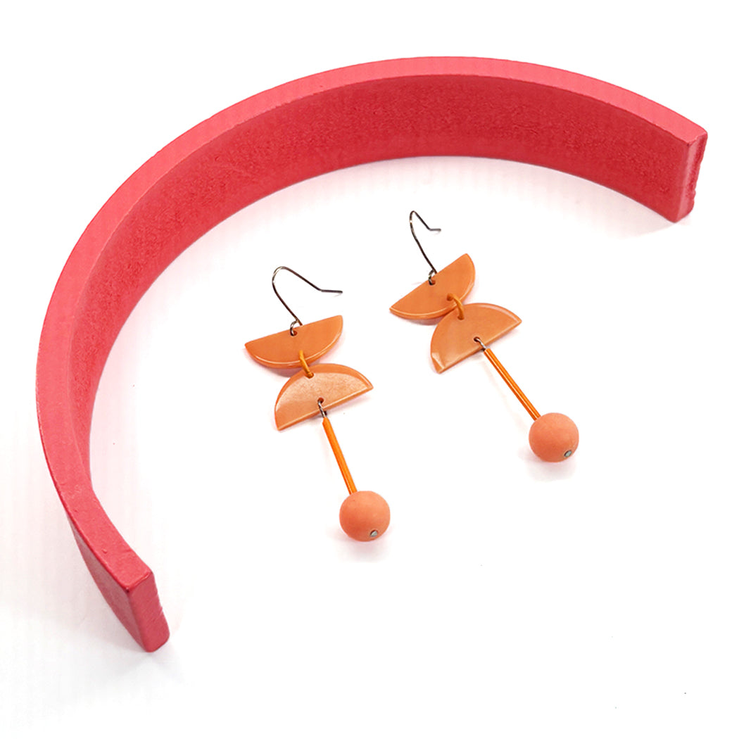 80s inspired peach dangle earrings inside a wood half circle on white background.
