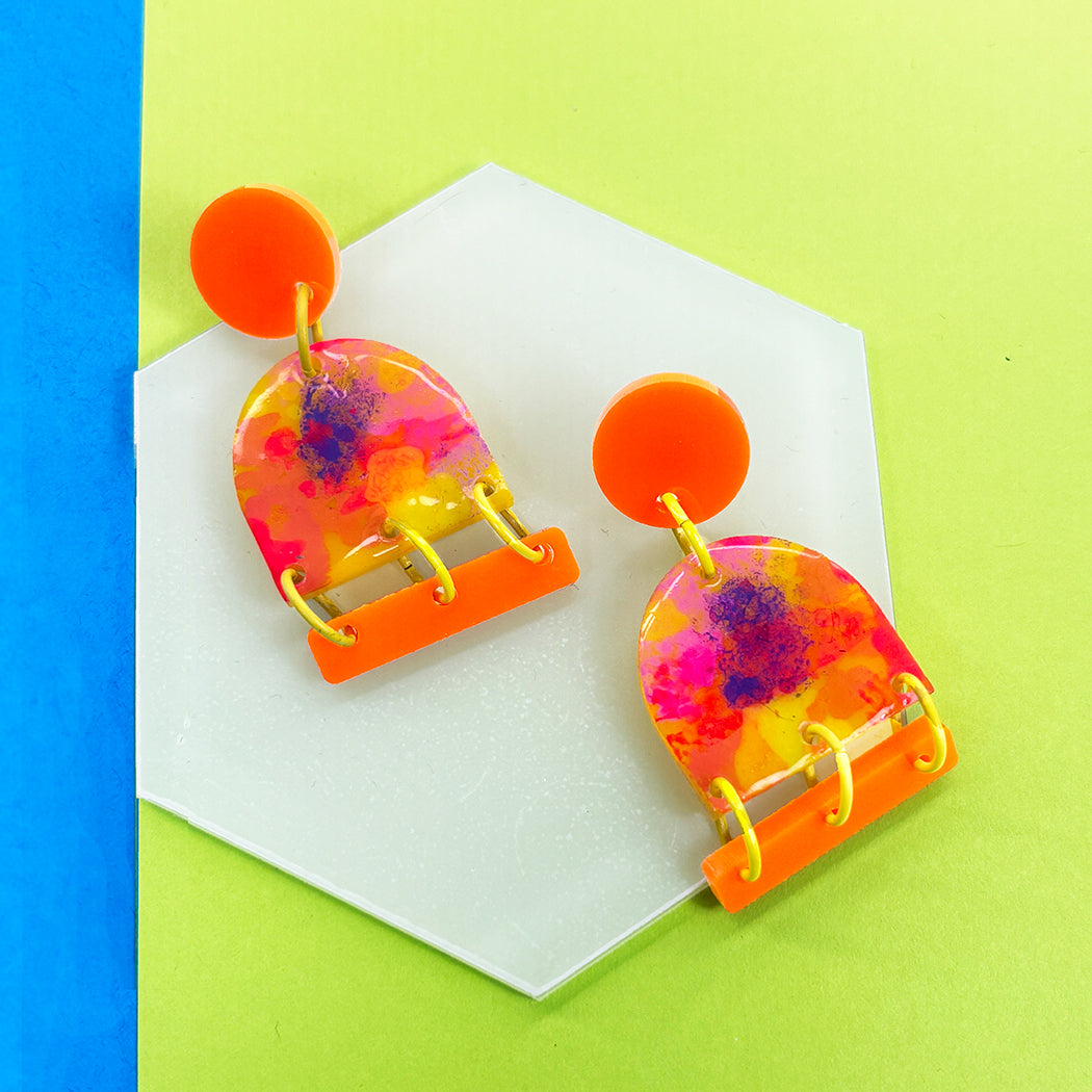 Bright orange, neon pink, neon yellow and purple Neon Impressionist earring on a white, spring green and blue background.
