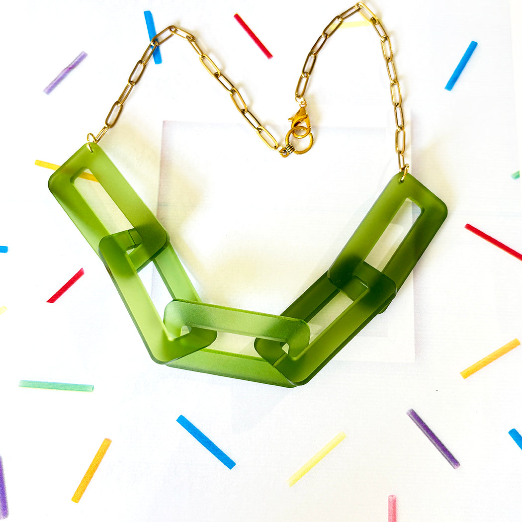 Green necklace with gold chain on a white background with colorful lines
