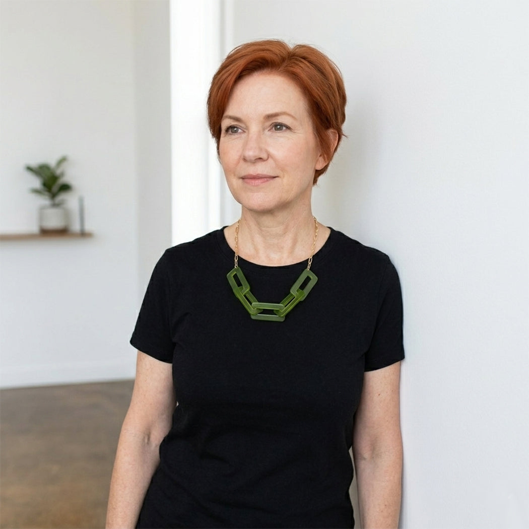Woman wearing a black t-shirt with a green necklace against a white wall.