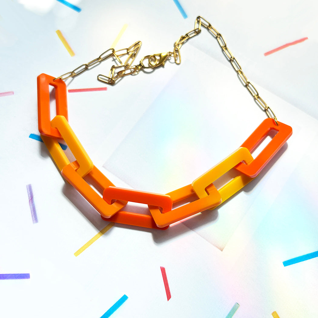 Colorful necklace with three different orange colored links, with goldtone chain on a multicolored background
