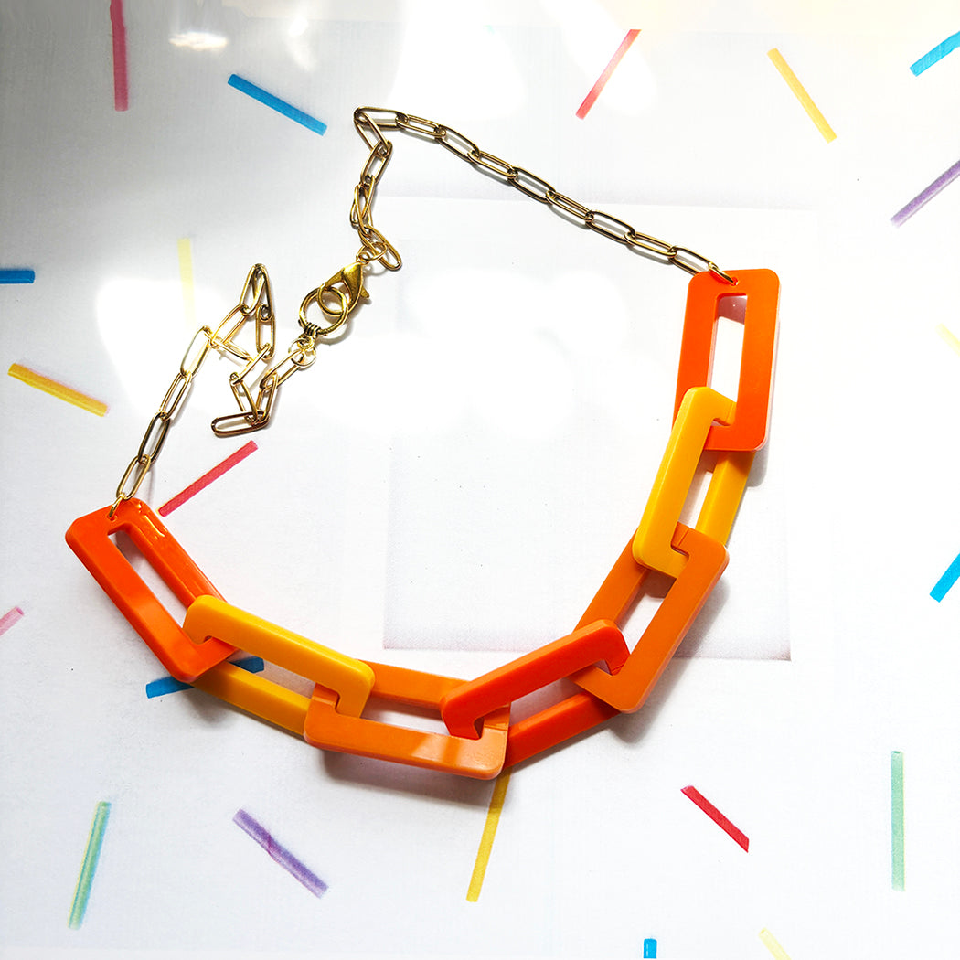 Necklace with orange links on a white background with colorful geometric shapes.