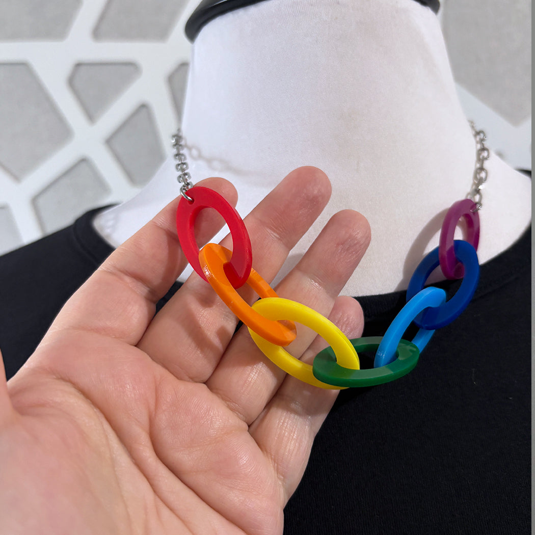 Rainbow colored large acrylic link necklace held by a hand against a neutral background