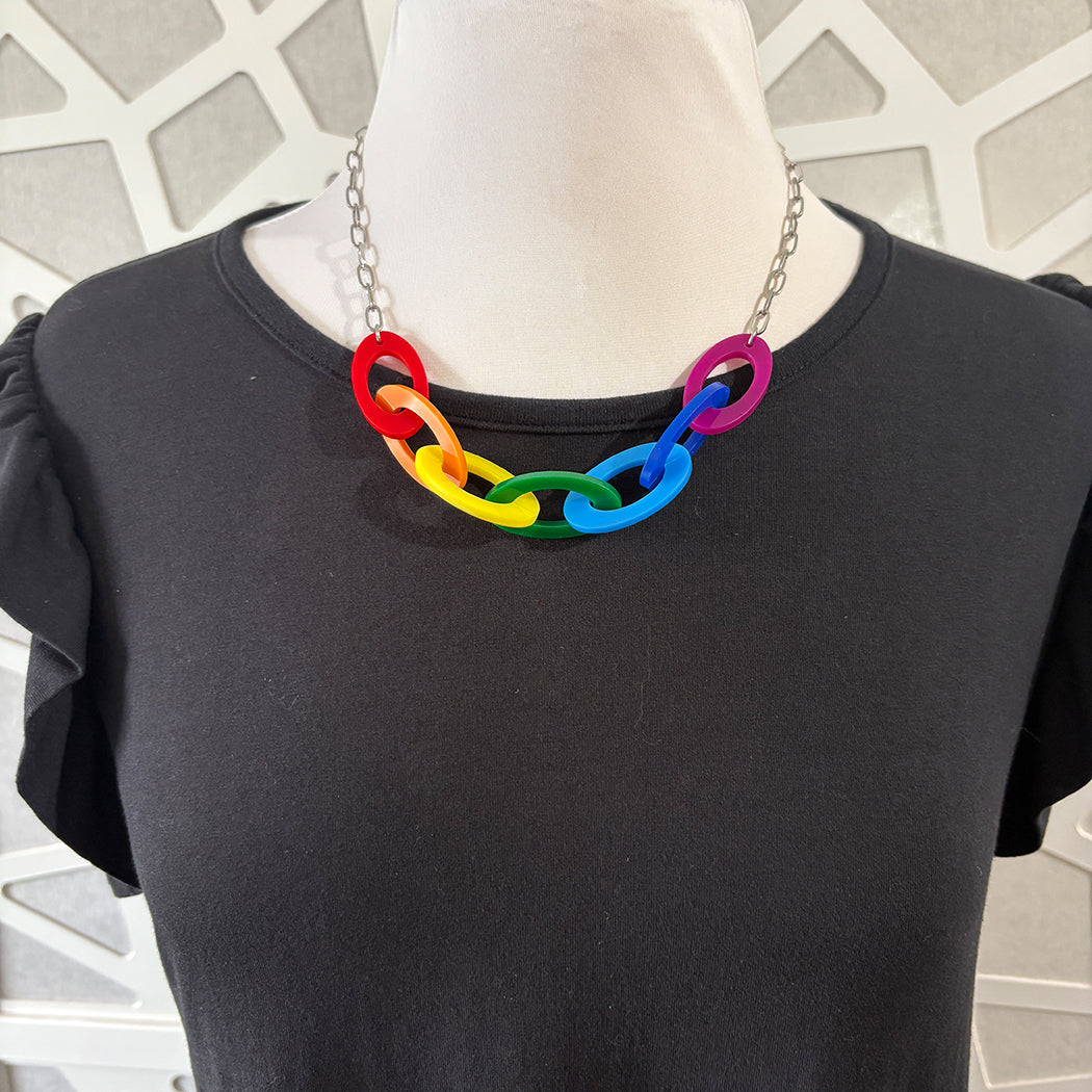 Mannequin wearing a black shirt with a colorful chain necklace against a geometric patterned wall.