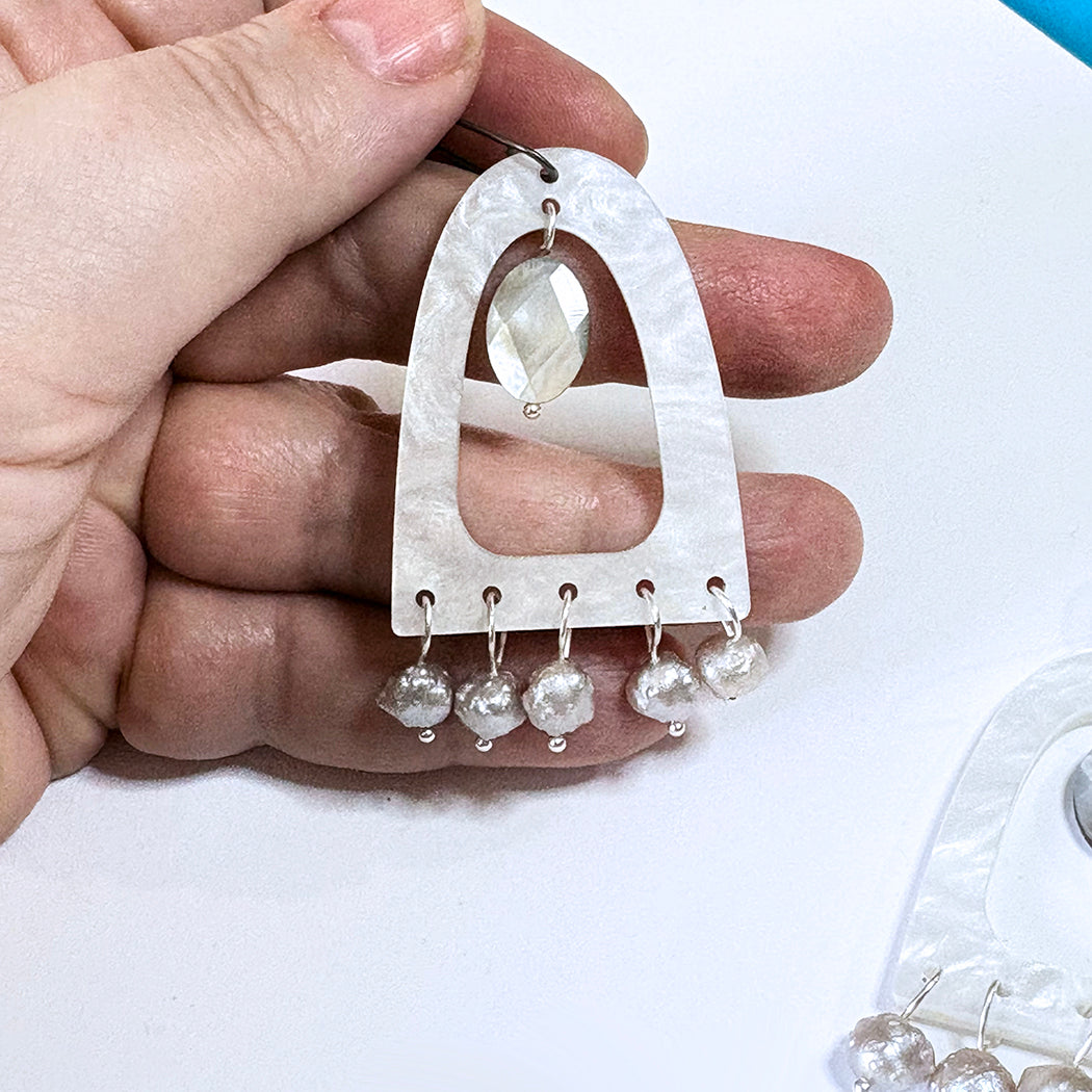 A hand holding pearl themed statement earring with five dangling druzy pearl beads, shown against a white background.