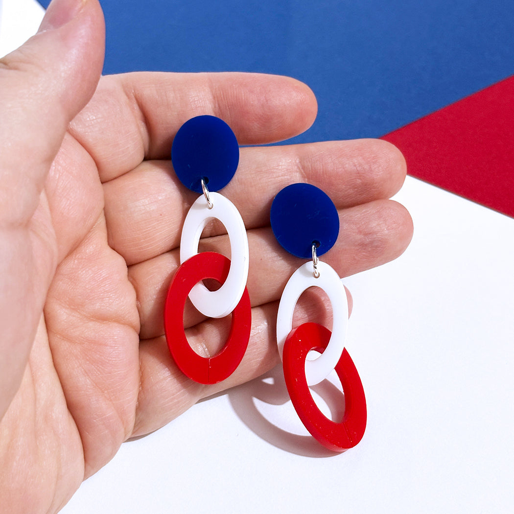 Red, white and blue link earrings held in a hand with a blue and red background