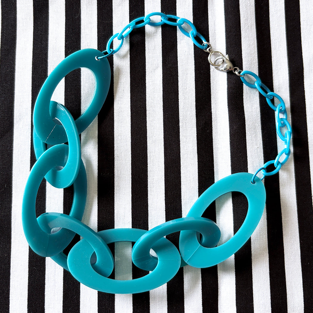 Teal acrylic chain necklace on a black and white striped background
